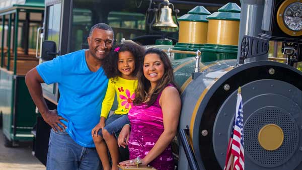 Two adults and a child smiling next to the trackless train at the Springs Preserve.
